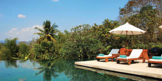 Infinity pool with two sunbeds and parasol on a poolside surrounded gardens