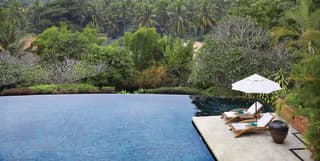 Two loungers and a white parasol are placed at the edge of the infinity pool, with cascading jungle and mountain views.
