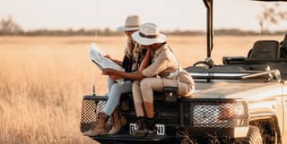 Two guests check a map while sitting on the front of the Belmond safari vehicle while out in the bush