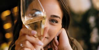 a young woman holding a glass of white wine