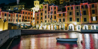 Coloured lights matching the walls of Portofino send reflections of pink, yellow and red on the harbour’s water at night