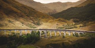 An arched stone rail viaduct curving across a mountainous valley