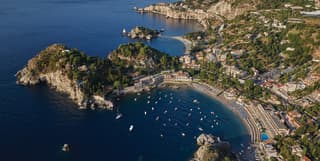Aerial view of yachts bobbing in Taormina bay with residences coating the hills
