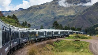 Blue and white train carriages curving under a cloud-coated Andean mountain