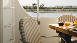 A chair with beige-striped cushions sits back from the breakfast table in a detail of al-fresco dining aboard the Pivoine.