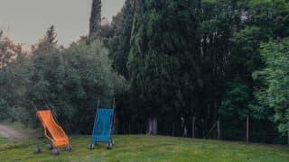 Two giant baby strollers with orange and blue fishing net seats by New York artist Nari Ward stand in the hotel's gardens