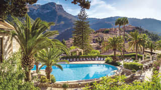 Outdoor hotel pool surrounded by palm trees overlooking the Tramuntana mountains