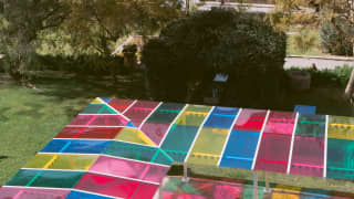 MITICO's pergola, with a translucent-panelled roof in red, pink, yellow, blue and green, throws a rainbow path on the grass.