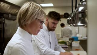 Ruinart's Chef in Residence, Valerie Radou, with short blonde hair and glasses, works alongside a male chef in the kitchen.