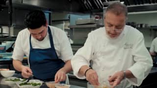 Chef Raymond Blanc, right, works with a chef, in a blue apron, in the kitchen, adding finishing touches to dishes by hand.
