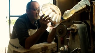 Glassmaker Sébastien Denizard holds a blown glass bowl against an etching machine, creating stunning, intricate patterns.