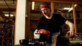 Glassblower Nicolas Diverchy, in a black top and red headband, makes a glass orange bowl in his Verrerie du Marais workshop.