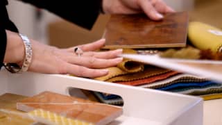A hand, belonging to Rachel Johnson, senior studio director at Wimberly Interiors, rests on fabric swatches and wood samples.