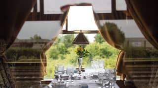 A window table is set for 4, with white tablecloth and elegant glassware. A single yellow rose sits centre in a silver bud vase