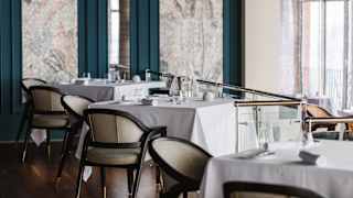 Eye-level view of three tables for two, with white cloths and napkins, in the teal and grey décor of William restaurant.