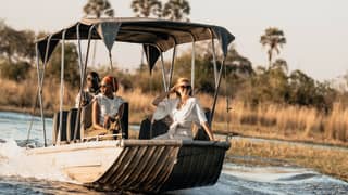 Stylish guests sitting at the bow of a motor boat sailing along a river among grasslands