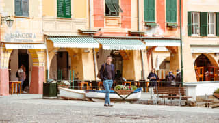 A man strolls across the harbour front cobbles. Green shutters are closed from the sun, against pale yellow and pink walls