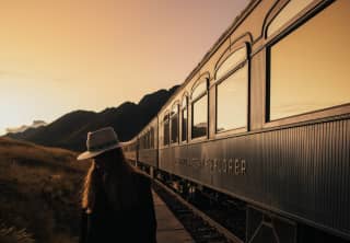 A woman with a fedora hat standing near the Andean Explorer at sunset