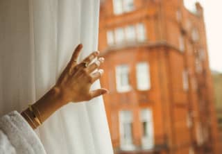 The hand of a female guest pulls back a curtain to reveal a view of the grand red-brick Victorian London townhouse opposite.