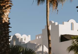 The villas' angular white walls form a geometric roofline with a blue sky backdrop and foreground palms.