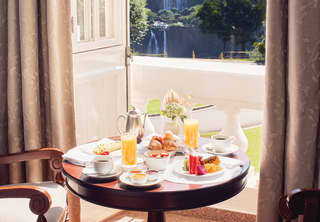Circular table laden with breakfast dishes next to a sunny balcony