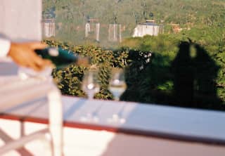 In soft-focus, two glasses on the terrace balustrade receive a top up of sparkling wine to be enjoyed with waterfall views.