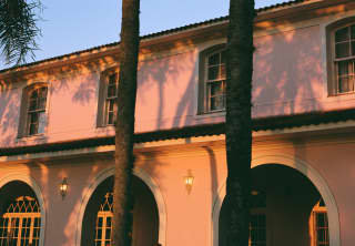Tall palms spill shadows on the pink exterior of the hacienda-style Hotel Das Cataratas, glowing in rosy early evening light.