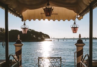 View of the glittering Venetian Lagoon along a stone pier with an awning and rose glass lanterns