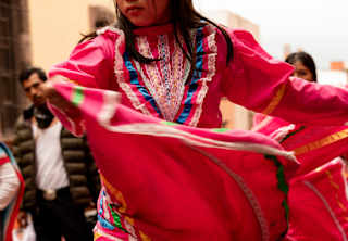 A woman swishes the wide skirt a red dress with green, white and blue embellishments as she dances to celebrate La Alborada.
