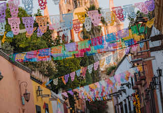 Angled image of the spires of Parroquia de San Miguel Arcángel rising behind a street fluttering with papel picado bunting.