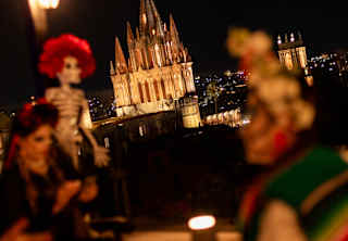 San Miguel's parroquia glows against the night sky, seen from a rooftop view over Dia de Muertos decorations in soft-focus.