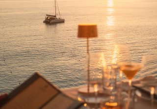 In soft-focus, an off-camera guest peruses the L'Oursin menu at an outside table, as the sun sets on the ocean horizon.