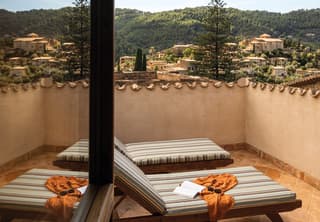 Teak sun loungers with striped cushions and a view over the hillside of Deià are reflected in the glass of an open window