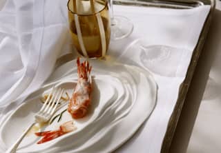 A half-finished dish of red prawns cooked in salt and served on an oyster shell-shaped plate rests on a cloth-covered tray.