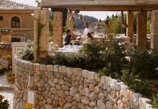 A waiter chats to guests on the terrace of Tramuntana Grill, seen from steps that wind in front of the supporting stone wall.