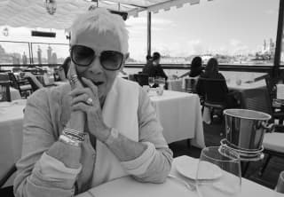 Black and white photo of actress, Dame Judy Dench, wearing dark glasses and silver jewellery, sitting at a table in Club Cip.