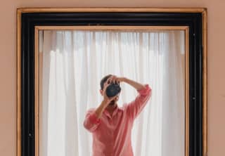 Seen in a mirror's reflection, Content Creation Manager, Marco Valmanara, wearing a pink shirt, holds a camera to his eye.