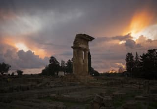 Jagged ruins at the Temple of Castor and Pollux in the Valley of Temples rise against a moody sky of sun and storm cloud.