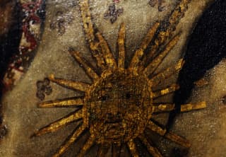 Close-up of a sun with a face, bristling with sunbeams, painted in gold on canvas, in an art detail.