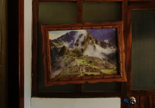 A photograph of Machu Picchu covered with floss-like clouds hangs lopsided in a wooden frame on a wall with glass panels.