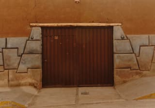 View of an old brown garage door set into an ochre-painted wall, surrounded by geometric-shaped stone bricks.