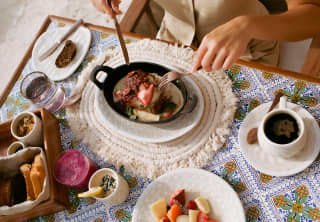 A guest of Casa Mayor tucks into Huevos Rancheros at a breakfast table with topped toast, coffee and a bowl of diced fruits.