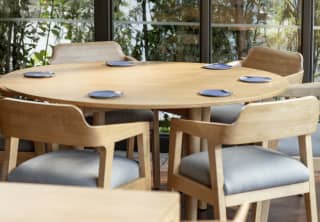 Looking over the pale wood dining tables and chairs to full length windows, offering a nature wall of forest views.