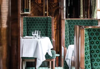 French polished wood panelling on walls and chair frames catches the light. Gilt framed mirrors feature zigzag art deco edges