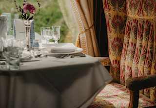 Soft window light falls on a dining table laid for guests and a padded, Art Deco beige and red chair, in a Gwen Car detail.