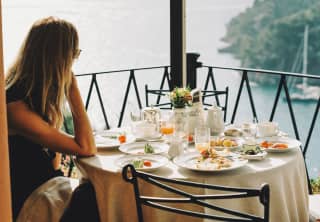 In the corner of the La Terrazza terrace, a woman sits at a table of finished plates and empty glasses, gazing at the view.