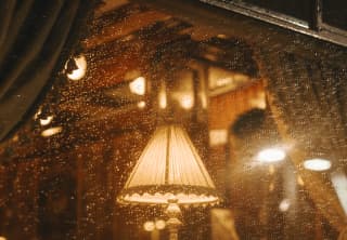 The inviting warmth of a table lamp in the dining car glows through the rain-spattered train window, seen from outside.