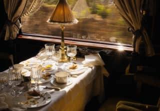 Sunlight settles on gold velvet seats at a window table, covered with finished plates and glasses in L'Oriental dining car.