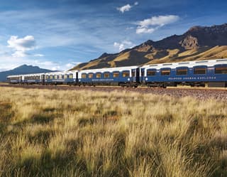 The Andean Explorer train racing across a Peruvian plain with mountains in the background