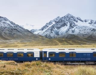 Two white and navy train carriages before snow coated Andean mountains
